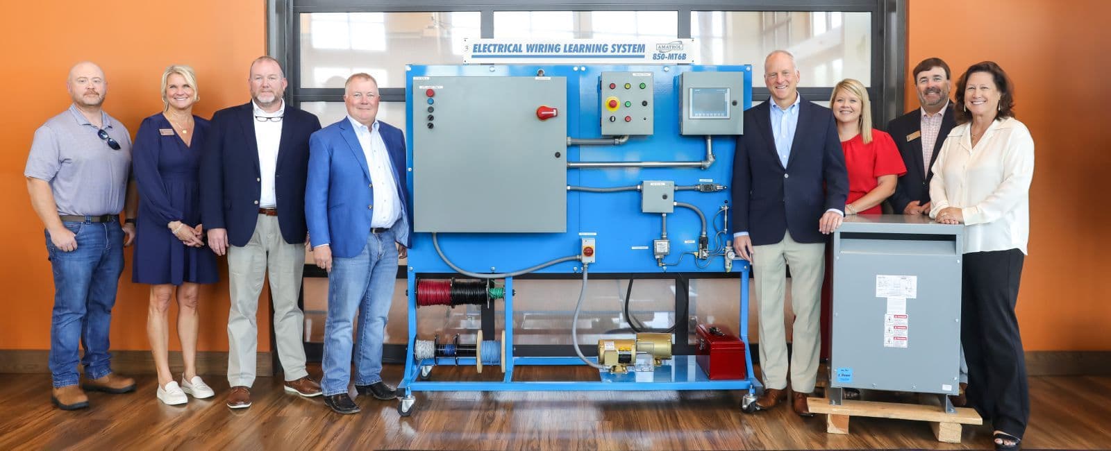 OTC staff and ACE Electric representatives stand beside a donated Amatrol electrical wiring training system.